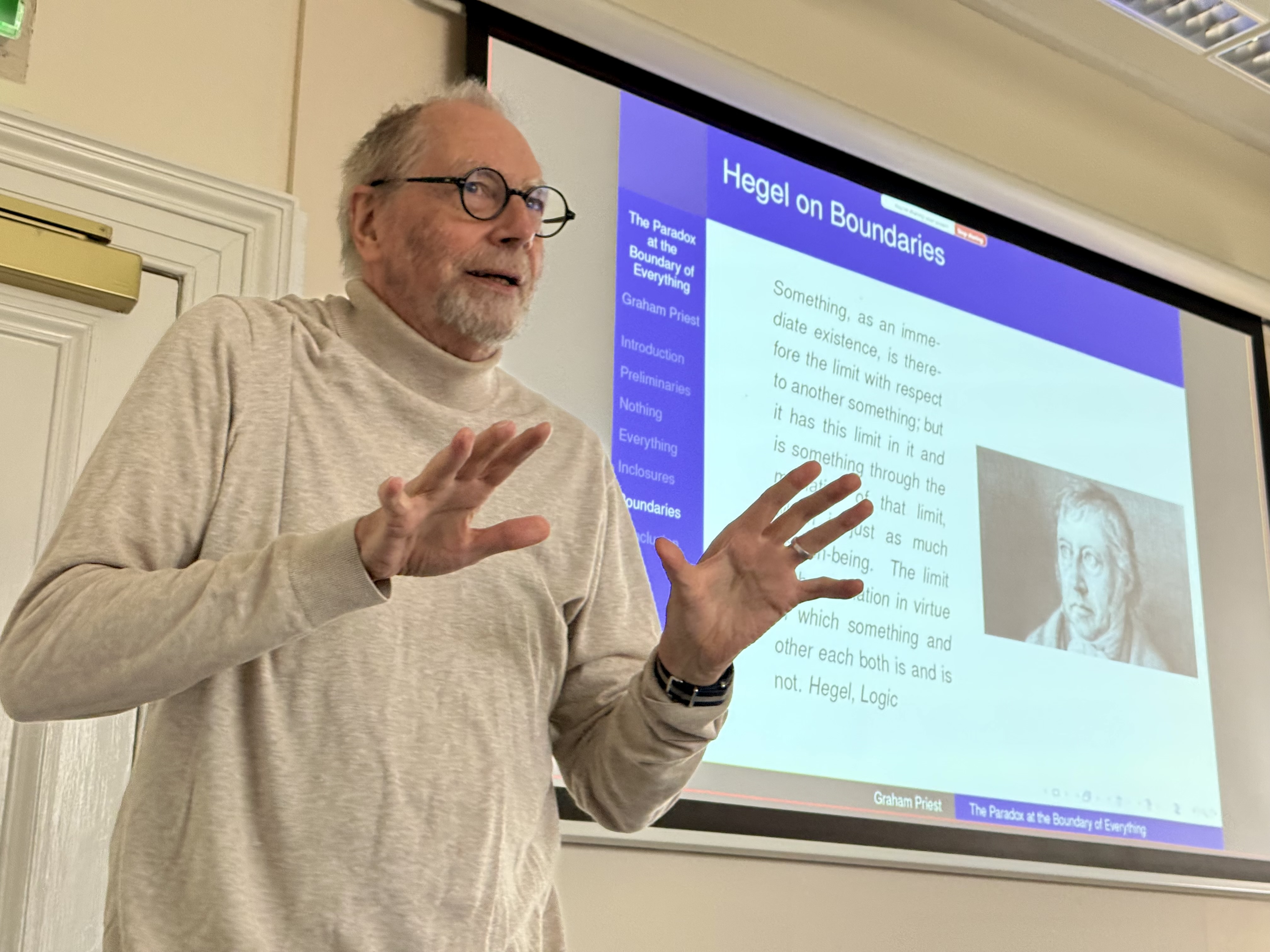 An older
bearded male white man (Prof. Graham Priest) standing on front of a digital
projection, upon which a quotation from Hegel's Logic can be seen.